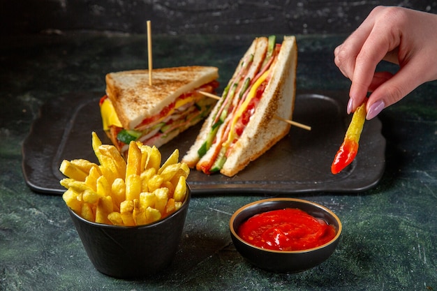 Vista frontal sabrosos sándwiches de jamón con papas fritas comiendo por la superficie oscura femenina