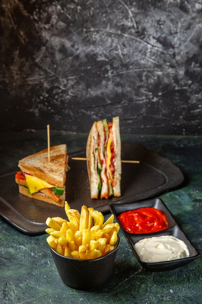 Vista frontal sabrosos sándwiches de jamón con papas fritas comiendo en una superficie oscura