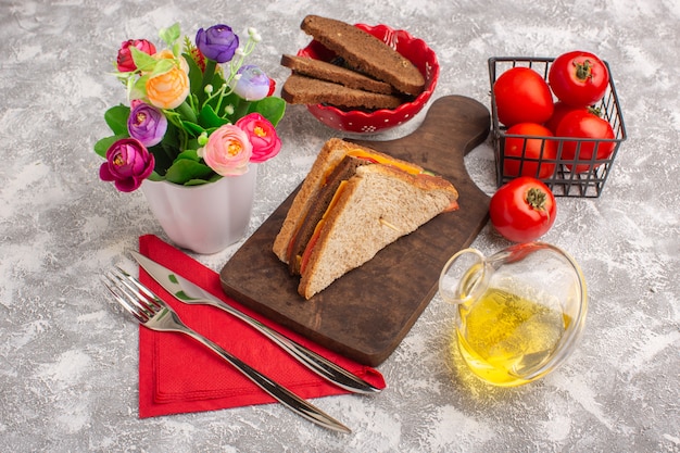 Vista frontal sabrosos sándwiches de tostadas con jamón de queso con aceite de tomates y flores en blanco