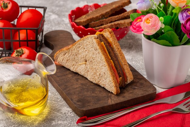 Vista frontal sabrosos sándwiches de tostadas con jamón de queso con aceite de tomates y flores en blanco