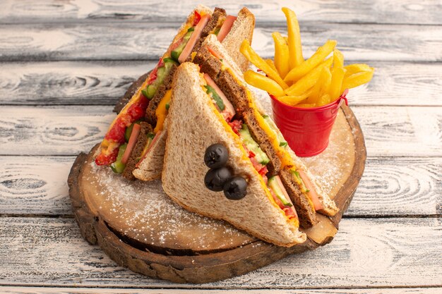 Vista frontal sabrosos sándwiches de tostadas con jamón de queso dentro con papas fritas en madera