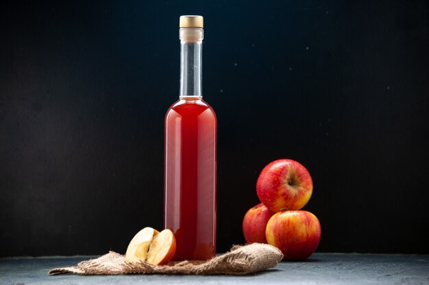 Vista frontal de la salsa de manzana roja en botella con manzanas frescas sobre una superficie oscura