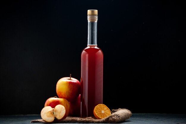 Vista frontal de la salsa de manzana roja en botella con manzanas frescas sobre una superficie oscura