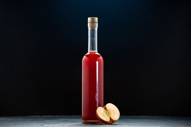 Vista frontal de la salsa de manzana roja en botella sobre superficie oscura