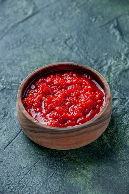 Vista frontal de la salsa de tomate dentro de la placa marrón sobre una mesa azul oscuro condimento de color rojo tomate pimienta sal