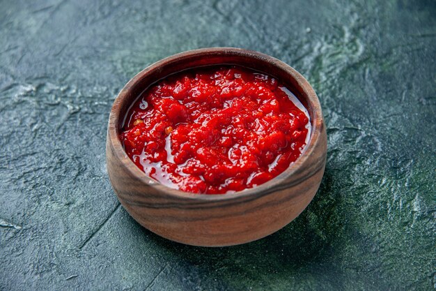 Vista frontal de la salsa de tomate dentro de la placa marrón sobre la superficie azul oscuro de color rojo tomate condimento pimienta sal