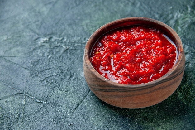 Vista frontal de la salsa de tomate dentro de la placa marrón sobre la superficie azul oscuro de color rojo tomate condimento pimienta sal