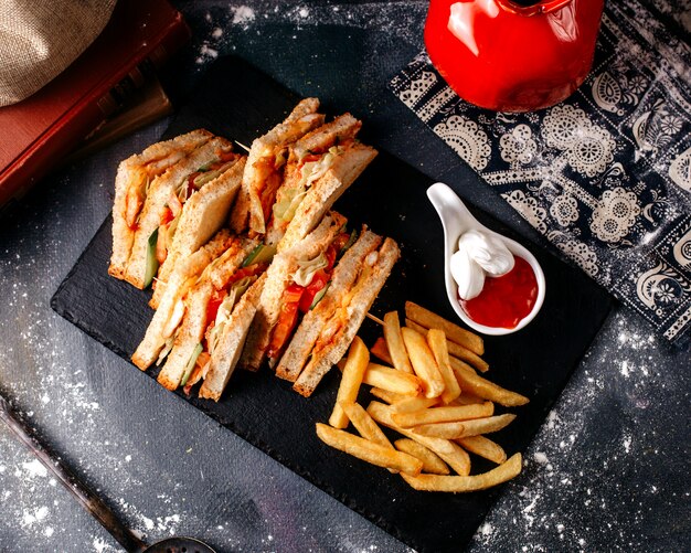 Vista frontal sándwich rebanadas sabrosas junto con papas fritas dentro de la placa negra en el piso gris