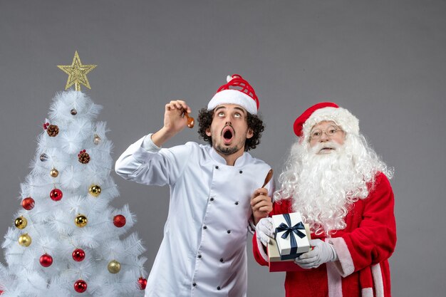 Vista frontal de santa claus alrededor del árbol de vacaciones con un cocinero masculino mirando los cielos