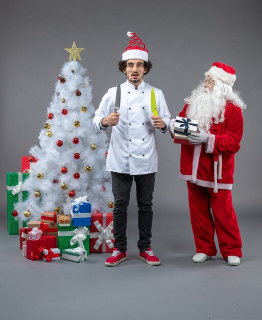 Vista frontal de santa claus alrededor de regalos de navidad con cocinero masculino