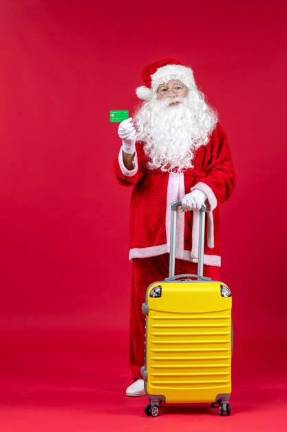 Vista frontal de santa claus con bolsa amarilla con tarjeta bancaria verde en la pared roja