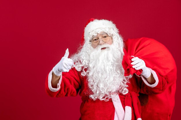 Vista frontal de santa claus con bolsa llena de regalos en el piso rojo vacaciones año nuevo emoción navideña