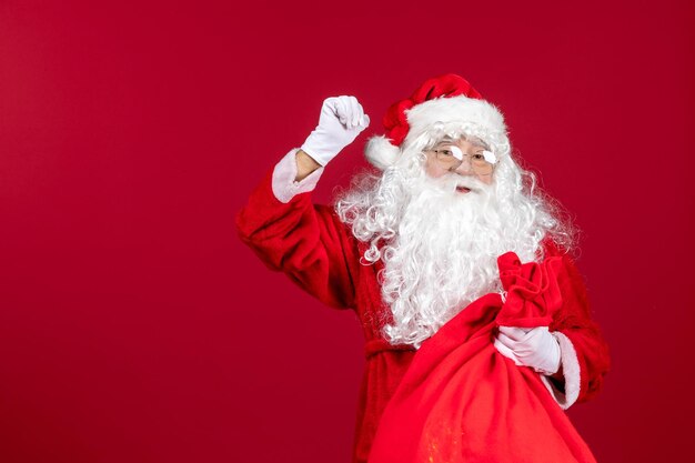 Vista frontal de santa claus con bolsa roja llena de regalos en la emoción de navidad de vacaciones de año nuevo rojo