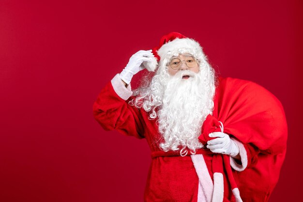 Vista frontal de santa claus con bolsa roja llena de regalos en el escritorio rojo emoción navideña año nuevo