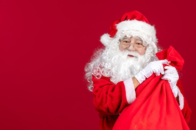 Vista frontal de santa claus con bolsa roja llena de regalos para niños en año nuevo rojo