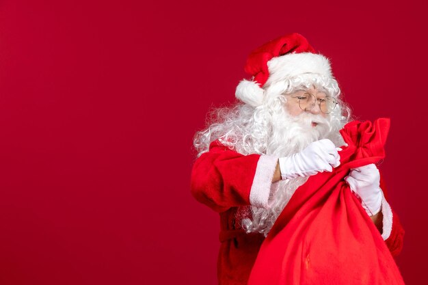 Vista frontal de santa claus con bolsa roja llena de regalos para niños en año nuevo rojo