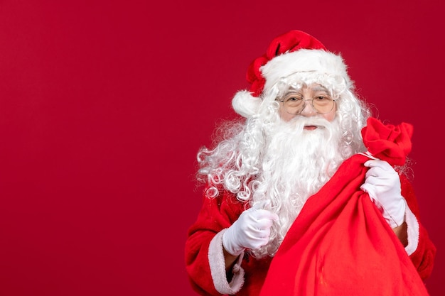 Vista frontal de santa claus con bolsa roja llena de regalos para niños en piso rojo