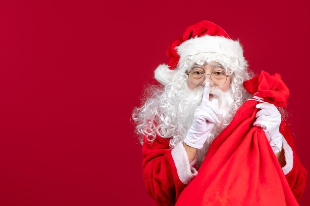 Vista frontal de santa claus con bolsa roja llena de regalos para niños en rojo