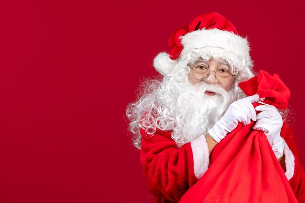 Vista frontal de santa claus con bolsa roja llena de regalos para niños en rojo