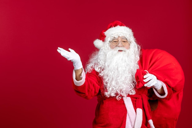 Vista frontal de santa claus con bolsa roja llena de regalos en rojo emoción año nuevo vacaciones de navidad