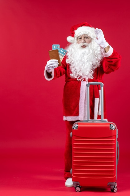 Vista frontal de santa claus con bolsa sosteniendo boletos y preparándose para el viaje en la pared roja