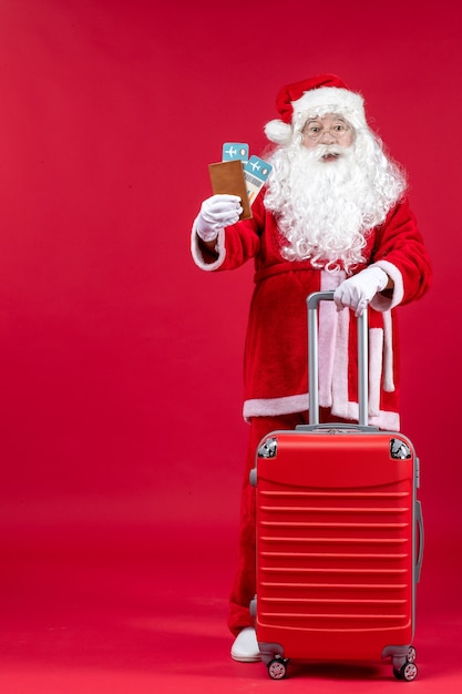 Vista frontal de santa claus con bolsa sosteniendo boletos y preparándose para el viaje en la pared roja