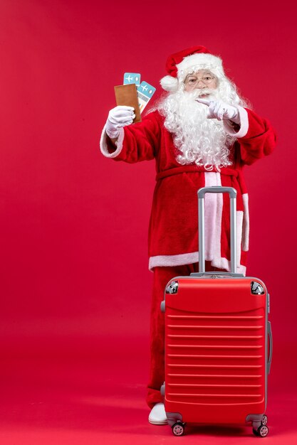 Vista frontal de santa claus con bolsa sosteniendo boletos y preparándose para el viaje en la pared roja