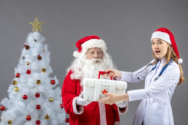 Vista frontal de santa claus con doctora que le dio botiquín de primeros auxilios en la pared gris