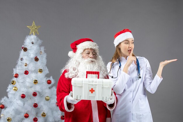 Vista frontal de santa claus con doctora que le dio botiquín de primeros auxilios en la pared gris