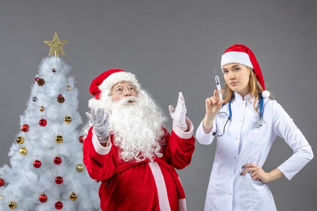 Vista frontal de santa claus con doctora que prepara la inyección en la pared gris