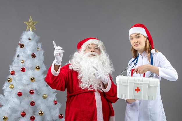 Foto gratuita vista frontal de santa claus con doctora que sostiene botiquín de primeros auxilios en la pared gris