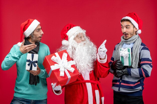 Vista frontal de santa claus con dos machos sosteniendo regalos en rojo regalo de año nuevo emoción navidad rojo