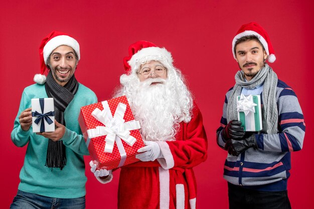 Vista frontal de santa claus con dos machos sosteniendo regalos en rojo regalo emoción navidad año nuevo rojo