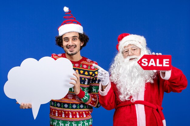 Vista frontal de santa claus con hombre joven con cartel blanco y escritura de venta