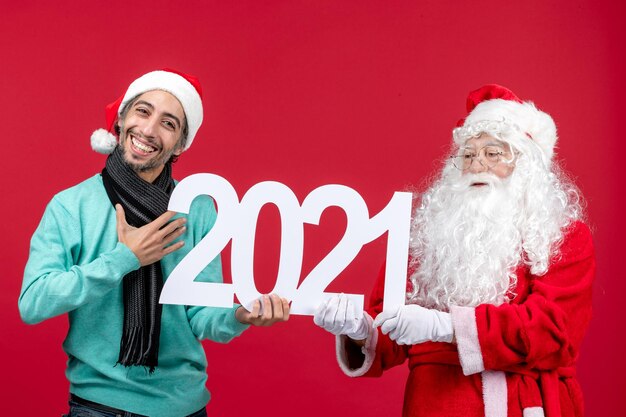 Vista frontal de santa claus con hombre joven sosteniendo la escritura en rojo año nuevo navidad vacaciones emoción presenta