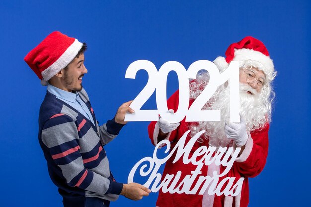 Vista frontal de santa claus con hombre joven sosteniendo y feliz navidad escritos en el año nuevo azul
