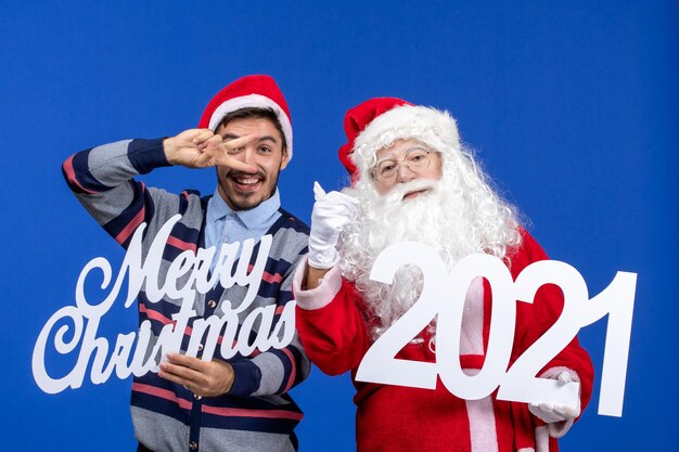 Vista frontal de santa claus con hombre joven sosteniendo y feliz navidad escritos en azul