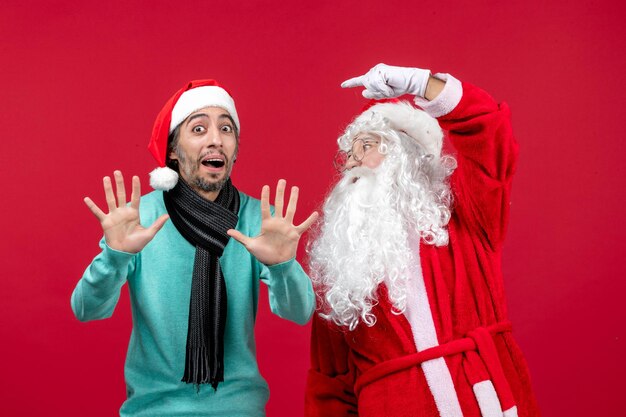 Vista frontal de santa claus con hombre parado en rojo navidad emoción regalos de vacaciones