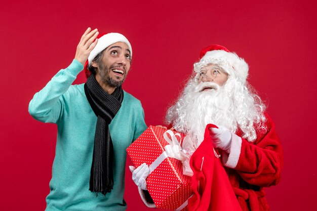 Vista frontal de santa claus con hombre sacando el presente de la bolsa en color rojo de emociones navideñas de vacaciones