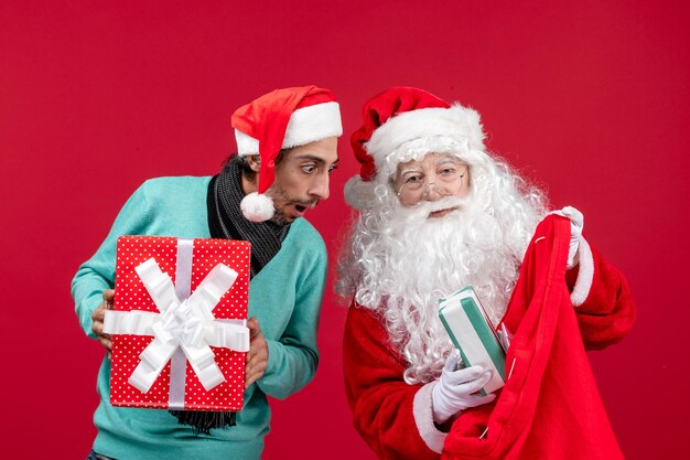 Vista frontal de santa claus con hombre sacando regalos de la bolsa en la emoción de navidad de regalo rojo