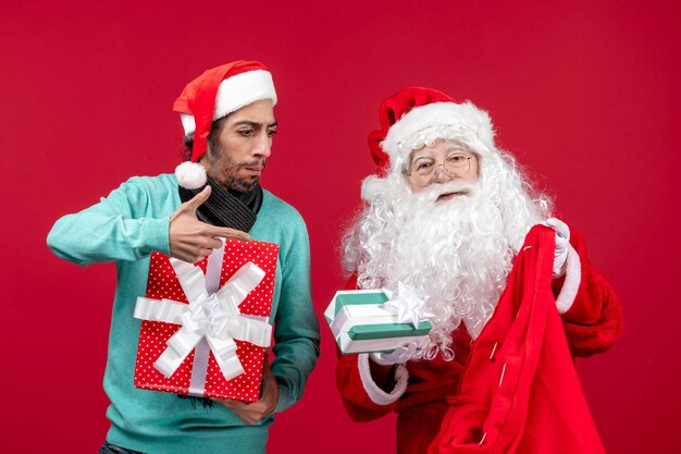 Vista frontal de santa claus con hombre sacando regalos de la bolsa en regalos rojos emoción de navidad rojo