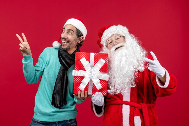 Vista frontal de santa claus con hombre sosteniendo presente de vacaciones en la emoción de regalo rojo navidad roja