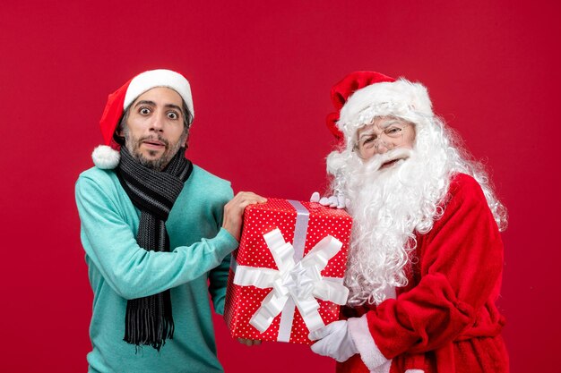 Vista frontal de santa claus con hombre sosteniendo presente de vacaciones en el regalo rojo rojo emoción de navidad año nuevo