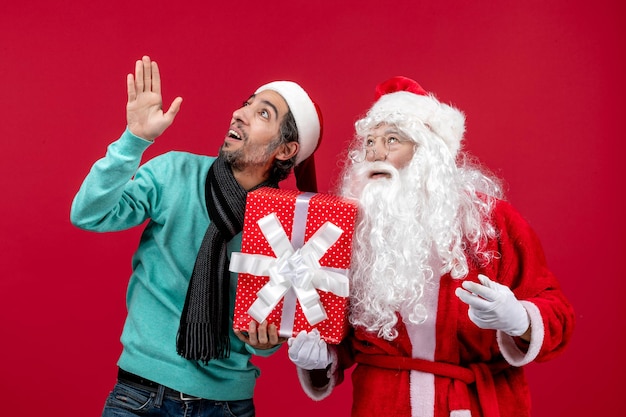 Vista frontal de santa claus con hombre sosteniendo presente de vacaciones en regalos rojos emoción rojo navidad año nuevo