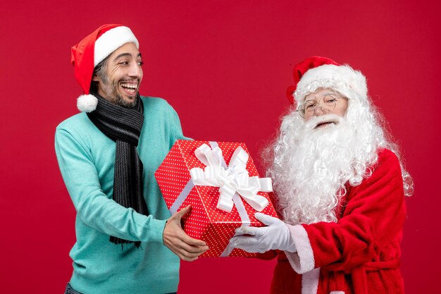 Vista frontal de santa claus con hombre sosteniendo presente de vacaciones en regalos rojos rojos emoción de navidad