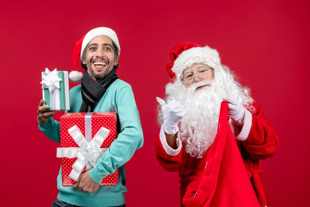 Vista frontal de santa claus con hombre sosteniendo regalos de bolsa en rojo regalo rojo emoción de navidad año nuevo