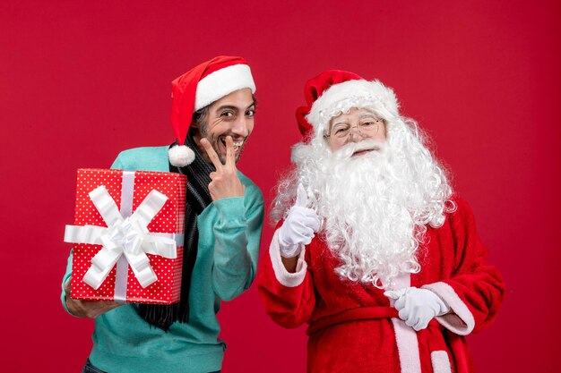 Vista frontal de santa claus con hombre sosteniendo vacaciones presente en escritorio rojo emoción regalo rojo navidad año nuevo