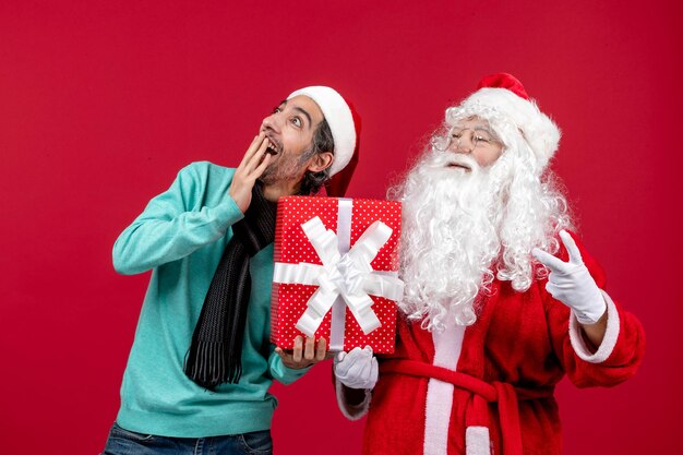 Vista frontal de santa claus con hombre sosteniendo vacaciones presente en escritorio rojo emoción regalo rojo navidad