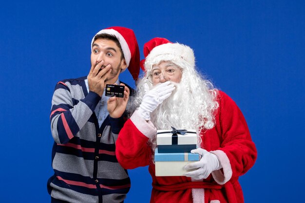 Vista frontal de santa claus con joven mirando sorprendentemente algo en la pared azul