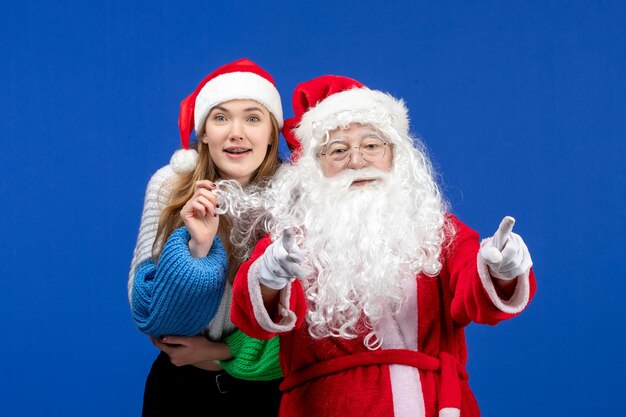 Vista frontal de santa claus con joven mujer bonita en la pared azul